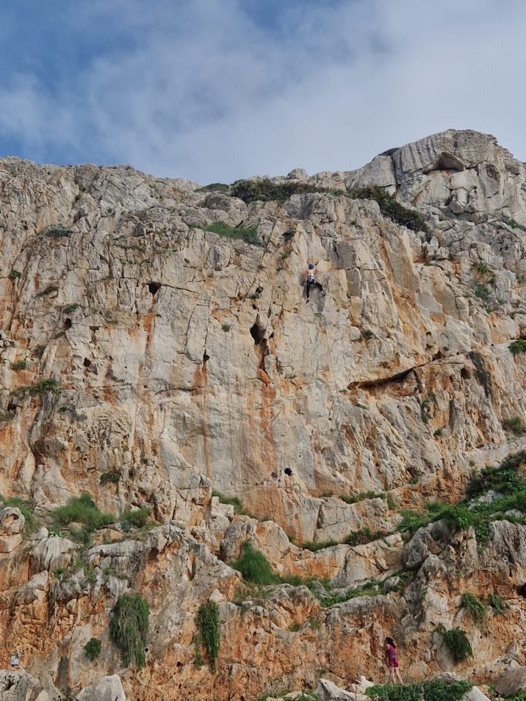 Skalista ściana wzniesienia, drobny zarys postaci, która się wspina po jej zboczu.